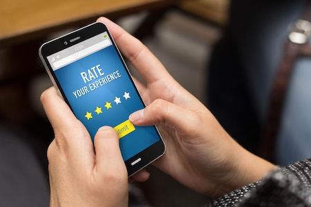 Customer using a smartphone to leave a positive hotel review to rate her experience.