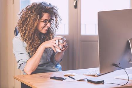 Young woman sitting in front of her computer with a cup of coffee setting up a Facebook event