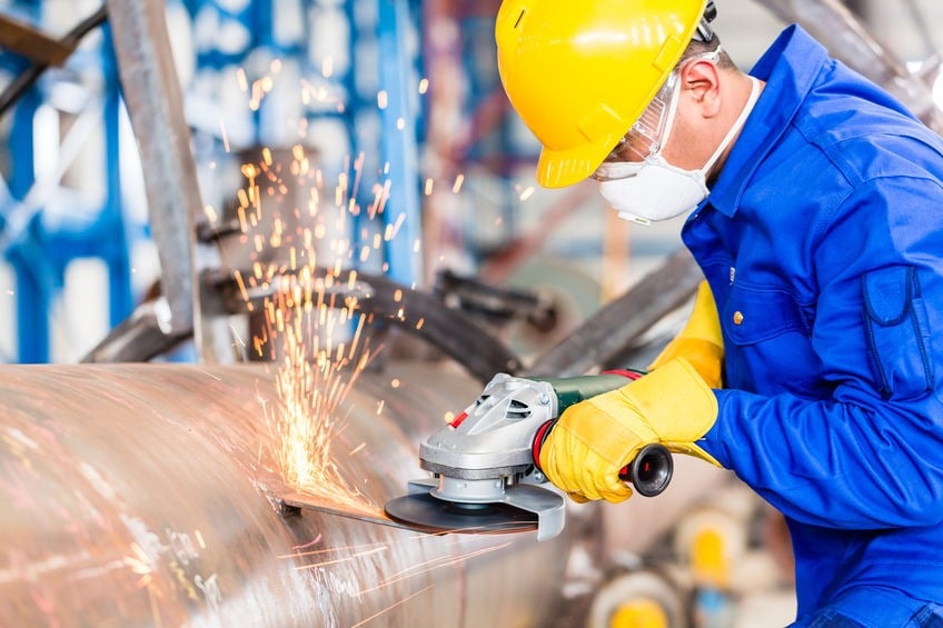 Metal worker in factory grinding metal of pipeline