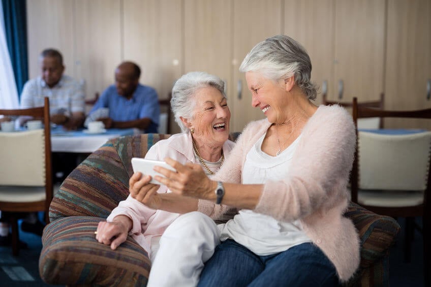 Happy senior woman taking selfie through mobile phone while sitting on sofa at nursing home