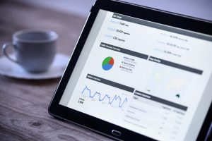 Charts and analytical data on the tablet screen with a cup of coffee on a wooden vintage table